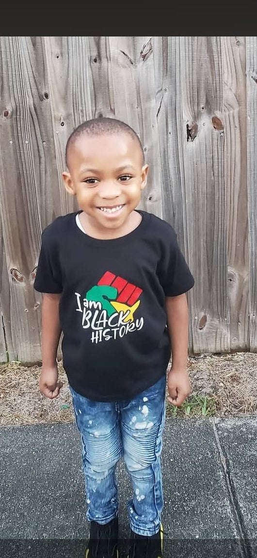 Child wearing a black t-shirt with a colorful graphic design, standing in front of a wooden fence.